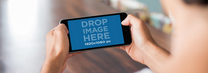 Mockup of a Man Holding an iPhone in Landscape Position with a Blurry Background 13042wide