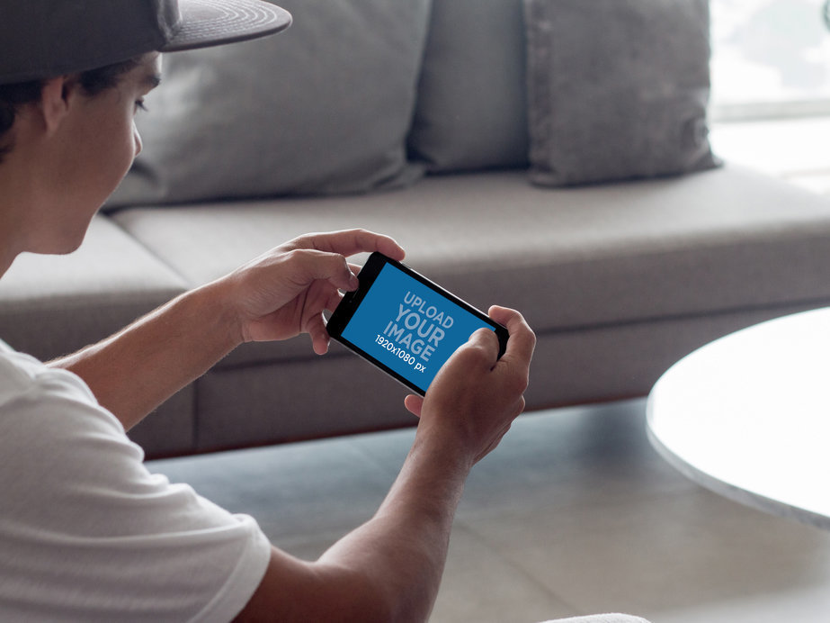 Mockup of a Teen Playing on his iPhone 7 Plus in Landscape Position in his Living Room