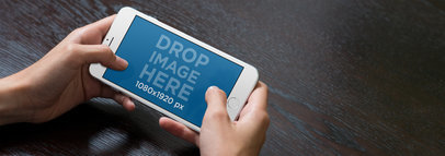 Teenager Holding a White iPhone 7 Plus Mockup in Landscape Position at a Table