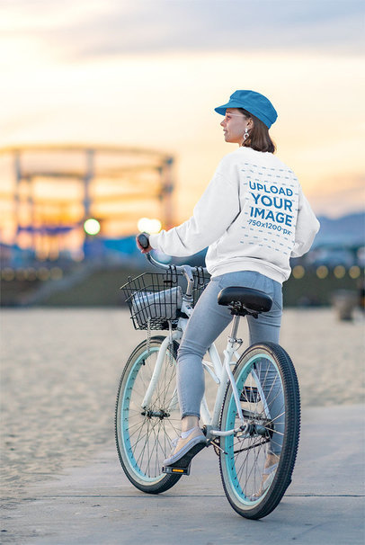 Mockup of a Young Woman with a Crewneck Sweatshirt Riding a Bike Outside 