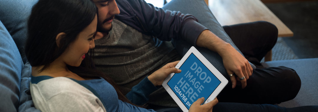  Mockup of a Couple Sitting in the Living Room Staring at an iPad in Landscape Position