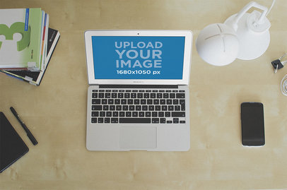 Mockup of a MacBook Air Placed over a Desk by Books and a Lamp