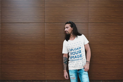 Mockup of a Man with Tattoos Wearing a Basic Tee by a Wooden Wall 