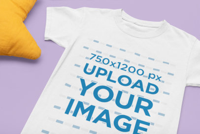 Mockup of a Flat Laid Kids' T-Shirt Placed Next to a Star-Shaped Pillow 33945