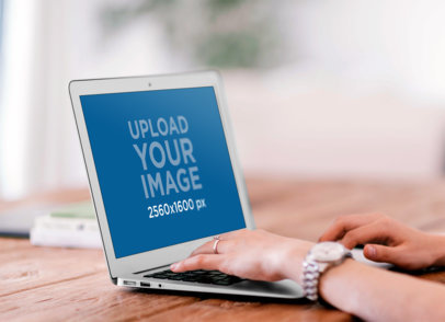 Mockup of a Woman Using a MacBook Air on a Wooden Table