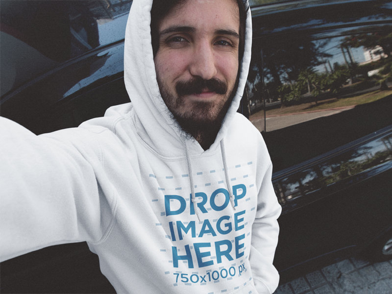 Hoodie Mockup Featuring a Young Man with a Beard Leaning Against a Car