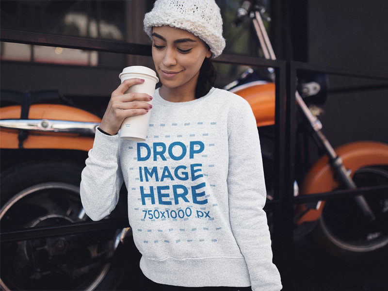 Young Woman with a Beanie and Heather Crewneck Mockup Having a Coffee in the Cold Against a Motorcycle