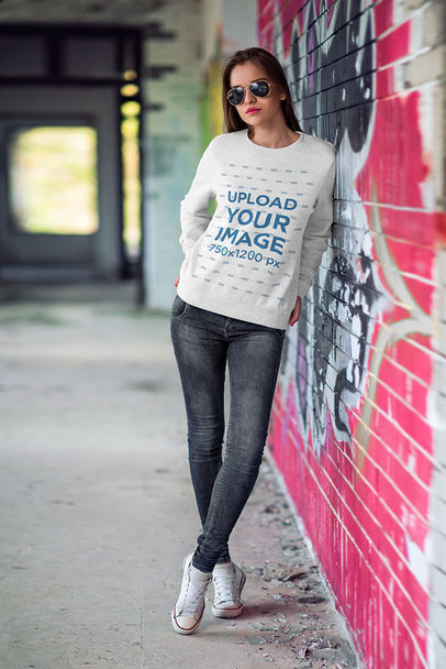 Mockup of a Woman Wearing a Heathered Crewneck Sweatshirt by a Graffiti Wall 