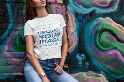 Mockup of a Woman in a T-Shirt Leaning on a Wall with Graffiti 