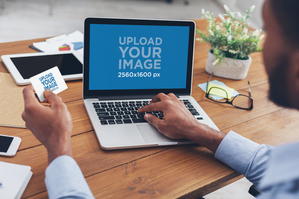 Over-the-Shoulder Mockup of a Man Working on His MacBook and Holding a Business Card