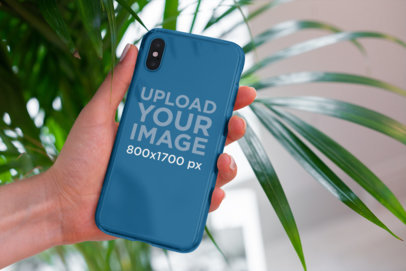 Mockup of a Woman Holding a Clear Phone Case in Front of a Houseplant