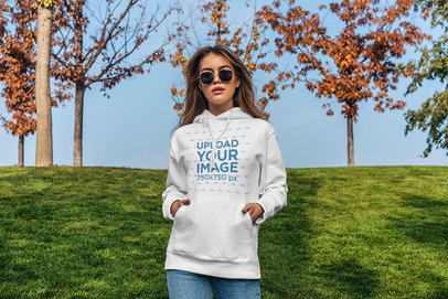 Pullover Hoodie Mockup of a Serious Woman Standing in Front of a Green Grass Hill