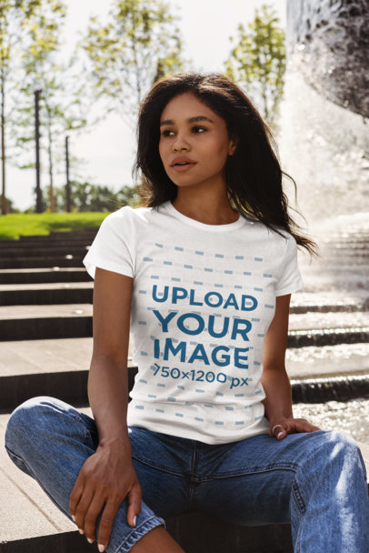 Mockup of a Woman Wearing a T-Shirt and Sitting by a Fountain 
