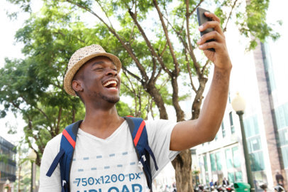 Mockup of a Man with a V-Neck Tee Taking a Selfie in the City 