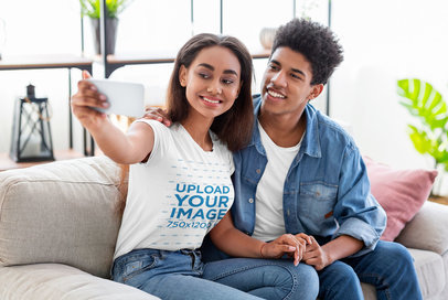 T-Shirt Mockup Featuring a Young Couple Taking a Selfie on a Couch