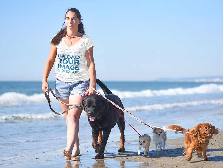 Mockup of a Woman with a V-Neck Tee Walking on the Beach with Her Dogs