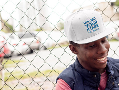 Snapback Hat Mockup of a Smiling Man Leaning on a Fence