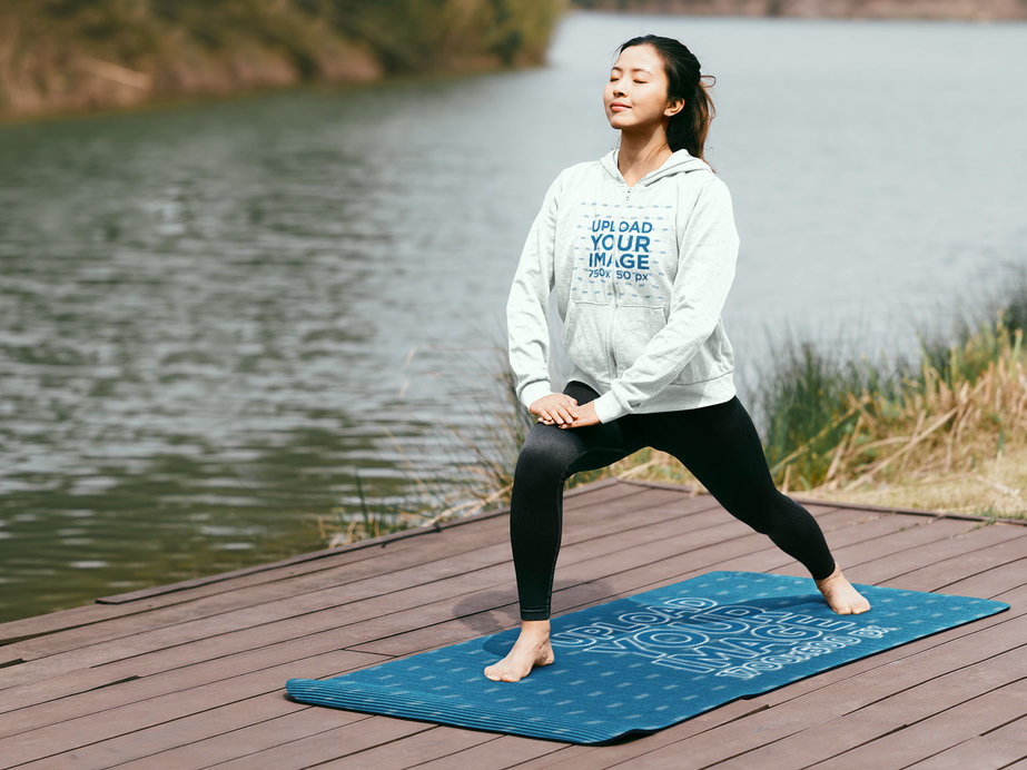 Full-Zip Hoodie Mockup Featuring a Woman by a Lake Practicing Yoga on a Mat 