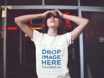 T-Shirt Mockup Of A Skinny Young Woman Grabbing Her Face While Smiling And Wearing a T-Shirt With Red Lights Behind