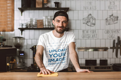 T-Shirt Mockup Featuring a Bearded Man Standing Behind a Cafe Counter 