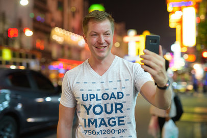 V-Neck T-Shirt Mockup of a Man Taking a Selfie on the Street