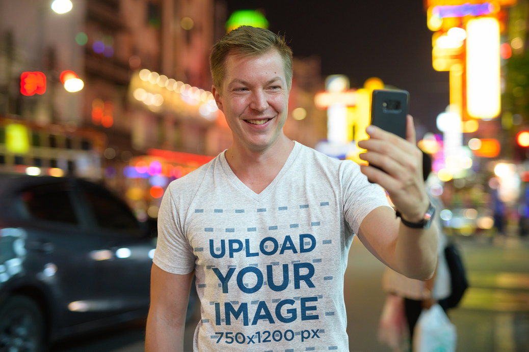 V-Neck T-Shirt Mockup of a Man Taking a Selfie on the Street
