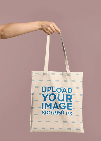 Mockup of an Arm Holding a Tote Bag In Front of a Colored Backdrop 41541-r-el2