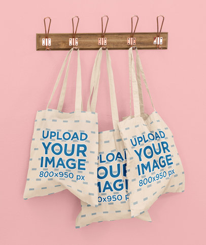 Mockup of Three Customizable Tote Bags Hanging Against a Solid Color Wall 41717-r-el2