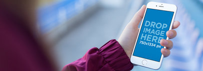 Mockup Template Of a Woman's Hand Holding an iPhone at a Stadium