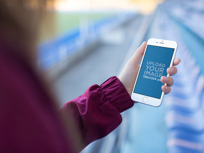 Mockup Template Of A Woman Holding An iPhone While Looking At A Blue Stadium