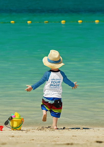 Back View Mockup of a Little Boy with a Raglan Long-Sleeve Tee Playing in the Beach