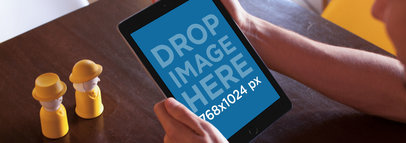 Mockup of an iPad Held by a Man Sitting down by a Wooden Table 14121w