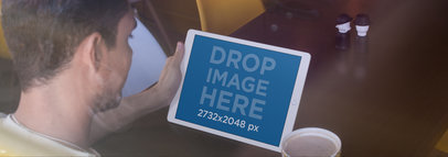 Through the Window Mockup of a Young Man Holding an iPad at a Cafe