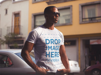 Young Man Wearing a Short Sleeved Round Neck T-Shirt and Sunglasses While Staring at the City Mockup