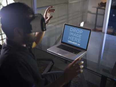 Mockup of a Young Man Wearing an Oculus Gear VR Device While His Macbook pro Is on the Desk a14246