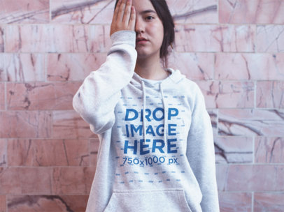 Asian Girl Putting Her Hand in an Eye While Wearing a Heather Pullover Hoodie Near a Pink Wall a12693