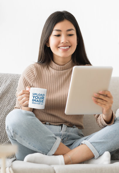 11 oz Mug Mockup Featuring a Woman with a Tablet on a Couch 