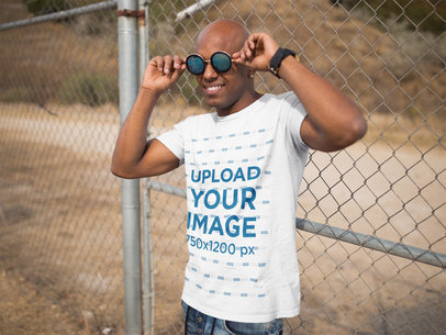 Smiling Dude Wearing a Short Sleeved Tshirt Template While Wearing Sunglasses Against a Fence Outdoors