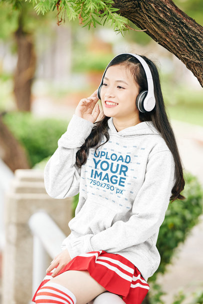 Mockup of a Teenager Wearing a Heathered Hoodie While Sitting in the Park