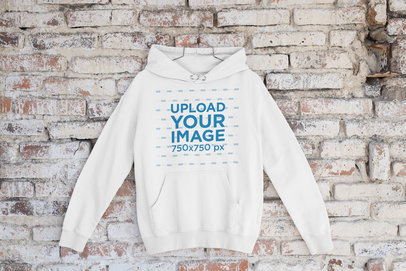 Mockup of a Pullover Hoodie Placed on a Hanger by a Brick Wall