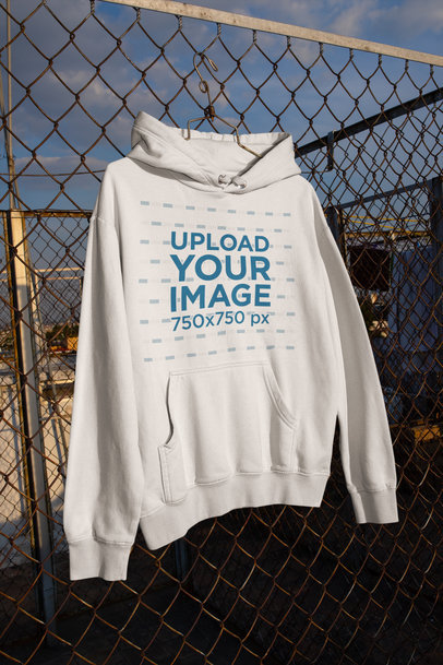 Mockup of a Pullover Hoodie Hanging from a Chainlink Fence m443