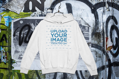 Mockup of a Pullover Hoodie Placed on a Hanger by a Graffiti Wall 