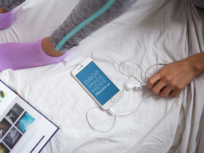 Girl With a White iPhone 6 Mockup Lying on a Bed With Earphones and a Book a14260