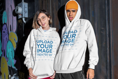 Mockup of a Man and a Woman Posing with Hoodies in an Urban Setting