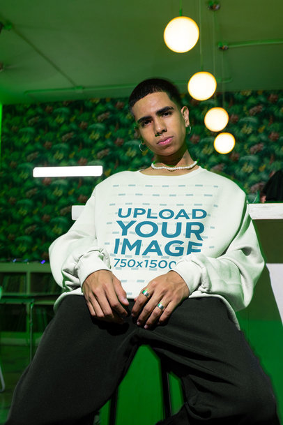 Sweatshirt Mockup Featuring a Serious Young Man Posing in a Room With a Green Light 