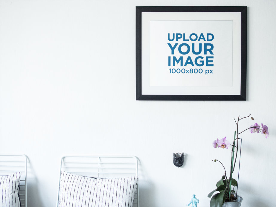 Art Print Mockup Frame on a White Wall Above Some Flowers and Chairs