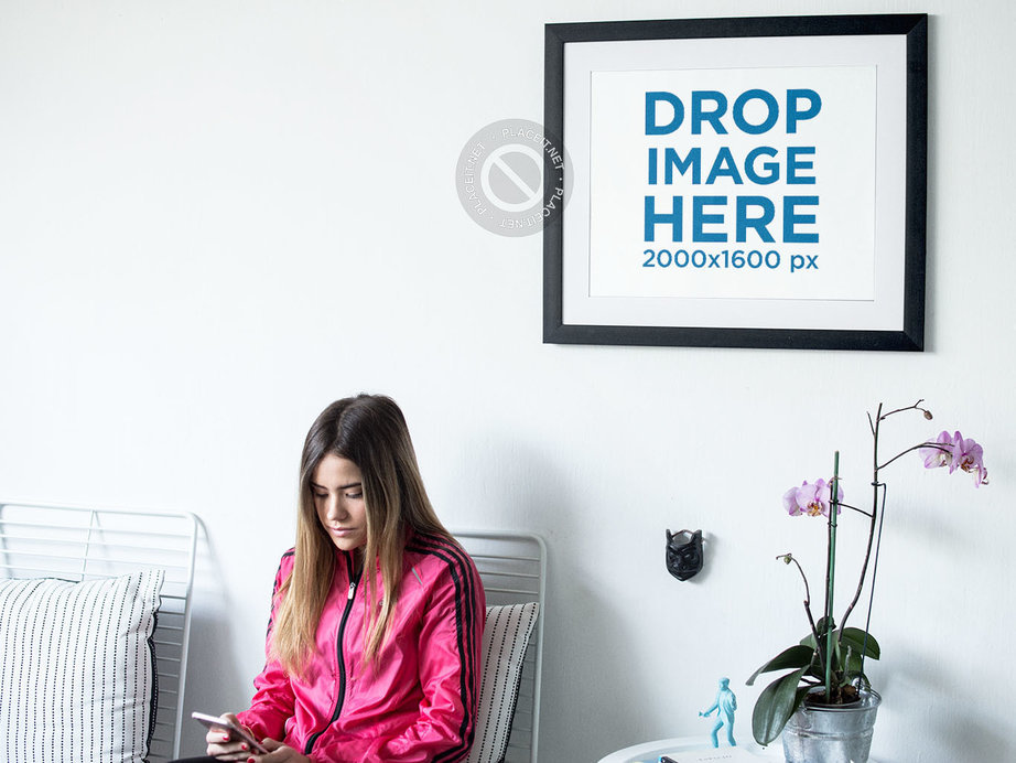 Young Woman Sitting Down Near a Framed Art Print Template on a White Wall