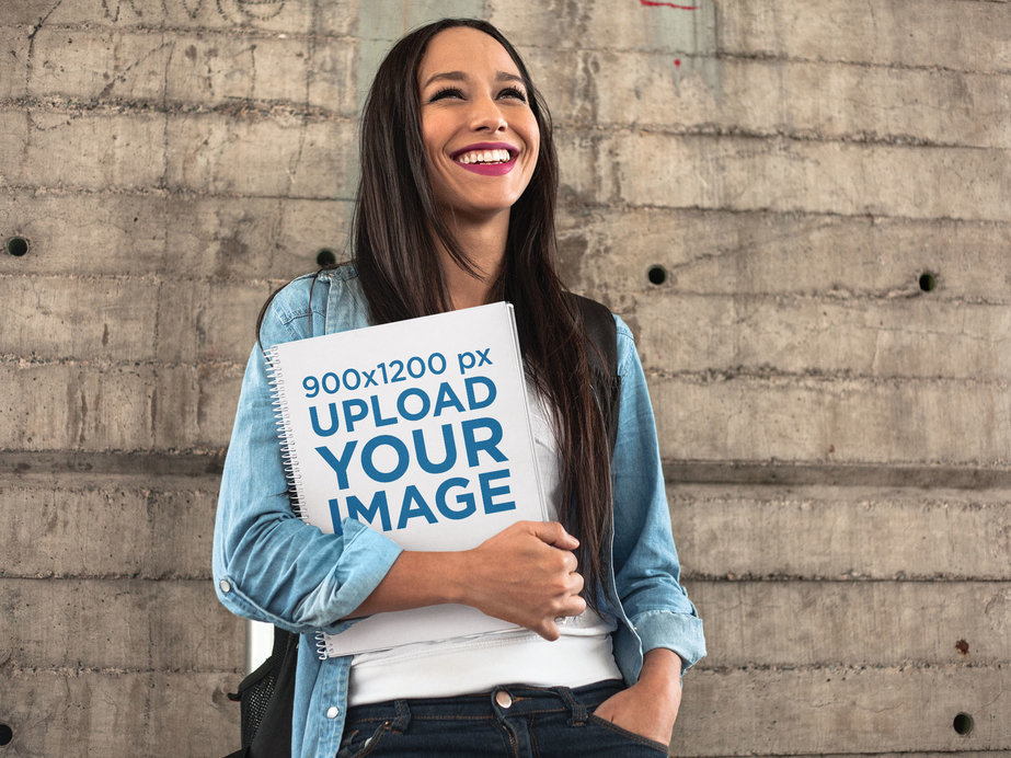 Happy Pretty Woman Holding a Spiral School Notebook Template While Against a Concrete Wall
