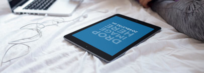 Mockup of an iPad in Portrait Position Laid on a Bed Next to a Laptop