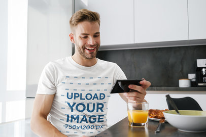 T-Shirt Mockup of a Man Checking His Phone While Having Breakfast 